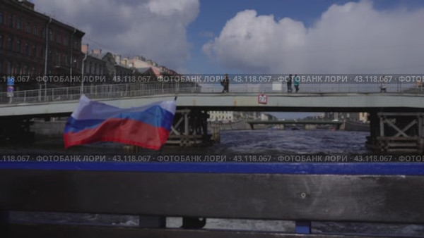 A pleasure excursion boat passes along the Fontanka River under the pedestrian bridge. View from the stern against the background of the Russian tricolor. Russia. St. Petersburg. 05/08/2024. Редакционное видео, видеограф Ярославский Максим / Фотобанк Лори