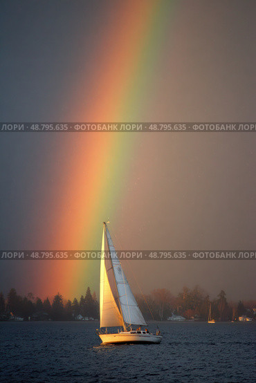 A rainbow is seen above a sailboat on a lake. Стоковое AI-изображение, AI-художник Ярославский Максим / Фотобанк Лори