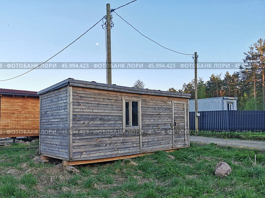 A rustic wooden cabin in a rural area under a clear blue sky with tall trees in the background. Стоковое фото, фотограф Александра Селина / Фотобанк Лори