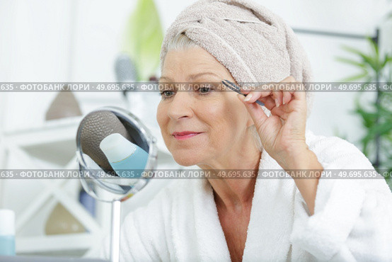 a senior woman plucking her eyebrows with tweezers. Стоковое фото, агентство Ingram Publishing / Фотобанк Лори