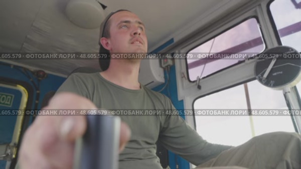 A skilled male crane operator is in the cabin of a large crane, expertly handling the joystick to maneuver the machine. He focuses intently, ensuring safety and precision as he moves heavy materials at a bustling construction site. Стоковое видео, видеограф Владимир Разгуляев / Фотобанк Лори