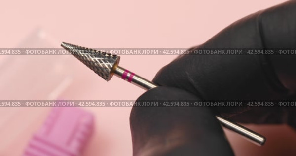 A specialist holds in his hands a carbide cutter for hardware manicure with a red notch on a pink background, close-up. Стоковое видео, видеограф Сергей Чайко / Фотобанк Лори