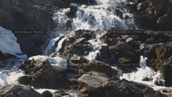 A stream of clear mountain water cascades down the rocks. A small waterfall in a mountainous area. The water foams and sparkles in the sun. The beauty of the wildlife. Front view. Стоковое видео, видеограф Воловодов Владимир / Фотобанк Лори