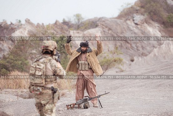 A Taliban soldier stands with a machine gun, Raise hands in surrender to the allied soldiers, In the desert mountain terrain battlefield. Стоковое фото, агентство Ingram Publishing / Фотобанк Лори