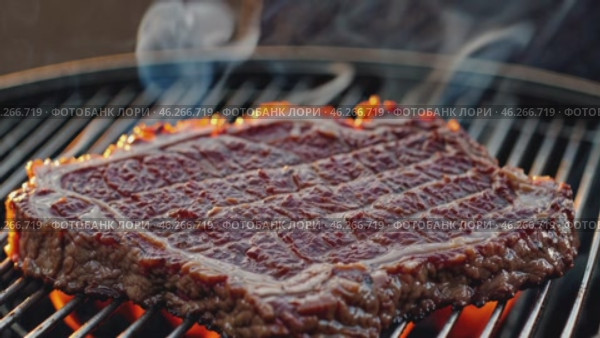 A thick, marbled steak with a rich glaze sizzles over an open-flame grill, with smoke rising as the meat sears, capturing the essence of barbecue cooking and mouthwatering grilled flavors. Стоковое AI-видео, аниматор Башкирова Анна / Фотобанк Лори