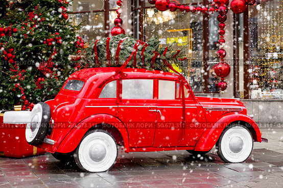 A vintage red Christmas car is carrying a Christmas tree on its roof. Decorated New Year's Moscow. Product delivery concept. Стоковое фото, фотограф Photojuli / Фотобанк Лори