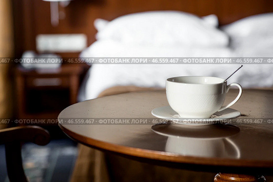 A white cup of hot tea or coffee on a wooden table in the interior of a hotel room. The concept of drinks and comfortable hotel accommodation. Стоковое фото, фотограф Photojuli / Фотобанк Лори