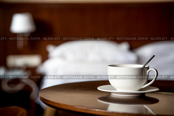 A white cup of hot tea or coffee on a wooden table in the interior of a hotel room. The concept of drinks and comfortable hotel accommodation. Стоковое фото, фотограф Photojuli / Фотобанк Лори