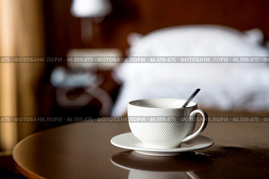 A white cup of hot tea or coffee on a wooden table in the interior of a hotel room. The concept of drinks and comfortable hotel accommodation. Стоковое фото, фотограф Photojuli / Фотобанк Лори