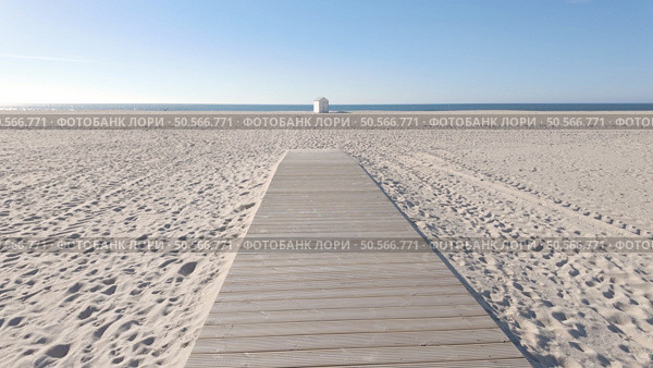 A wide wooden walkway stretches across a vast, pristine beach, leading towards a small white lifeguard tower under a clear blue sky. Стоковое фото, агентство Ingram Publishing / Фотобанк Лори