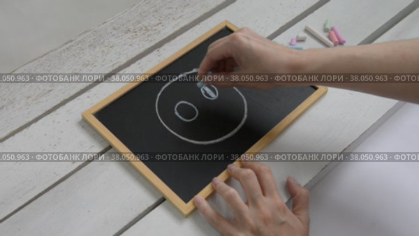 A woman draws a face with a smile on a table with chalk on a children's blackboard. Стоковое видео, видеограф Катерина Белякина / Фотобанк Лори