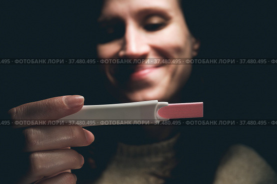 A woman in a dark room looks at the result of a pregnancy test and smiles. Стоковое фото, фотограф Александр Кириллов / Фотобанк Лори