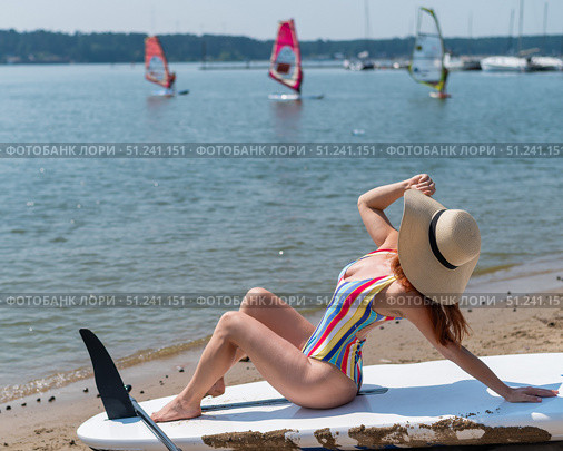 A woman in a swimsuit and a hat is posing on a sup board on the beach. Стоковое фото, фотограф Михаил Решетников / Фотобанк Лори
