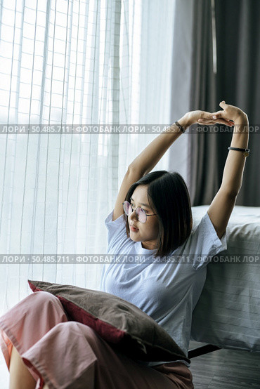 A woman in a white shirt sitting on the bed and raising both arms. Стоковое фото, агентство Ingram Publishing / Фотобанк Лори