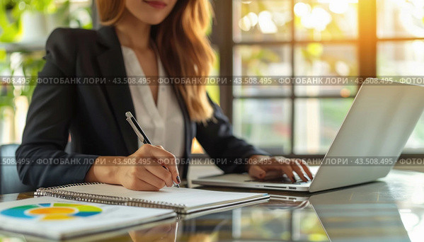 A woman is sitting at a desk, using a laptop, and jotting down notes in a notebook. Стоковое AI-изображение, AI-художник Юрий Поздников / Фотобанк Лори