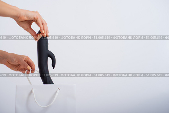 A woman makes a purchase and puts a dildo in a bag on a white background. Close-up of female hands with a black vibrator. Стоковое фото, фотограф Михаил Решетников / Фотобанк Лори