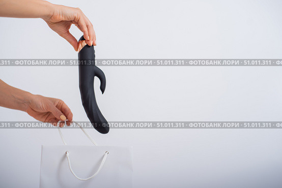 A woman makes a purchase and puts a dildo in a bag on a white background. Close-up of female hands with a black vibrator. Стоковое фото, фотограф Михаил Решетников / Фотобанк Лори