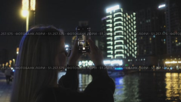 A woman photographs a vibrant city skyline at night, capturing its beauty. Стоковое видео, видеограф Cantemir Dumitru / Фотобанк Лори