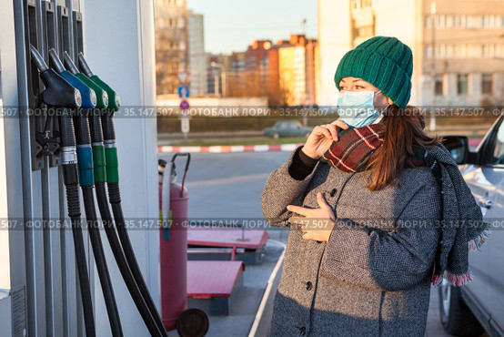 A woman with protective mask remembers brand of fuel at a gas station for her car. Looking at several nozzles with regular petrol and diesel. Стоковое фото, фотограф Кекяляйнен Андрей / Фотобанк Лори