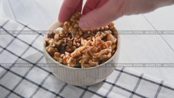 A woman's hand takes a peeled walnut kernel from a bowl filled with walnuts, preparing to enjoy a nutritious and delicious snack rich in protein and healthy fats. Стоковое видео, видеограф Ольга Ильина / Фотобанк Лори