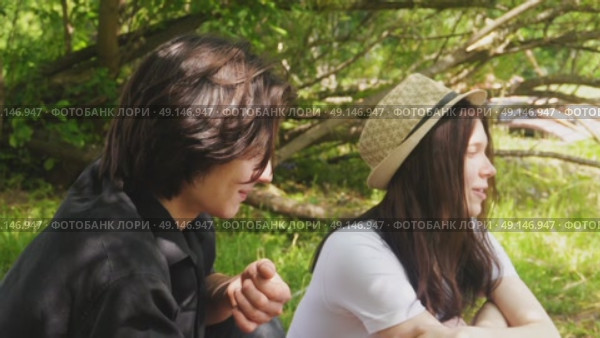 A young couple is sitting in the shade of bushes on a summer afternoon. Стоковое видео, видеограф Ярославский Максим / Фотобанк Лори