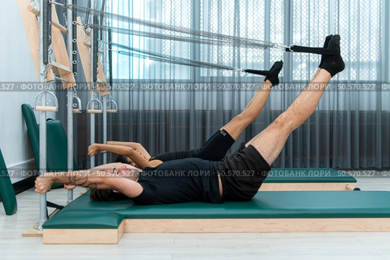 A young man and a young woman are doing pilates exercises on a pilates reformer. Стоковое фото, агентство Ingram Publishing / Фотобанк Лори