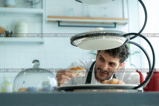A young man puts on an apron to make dessert to eat with his wife. Checking the completeness of the finished dessert. Стоковое фото, агентство Ingram Publishing / Фотобанк Лори