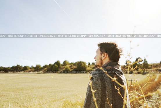 A young man standing from back enjoying in calm the morning autumn sun in a path of a yellow field with the backlight from the blue sky. Стоковое фото, агентство Ingram Publishing / Фотобанк Лори