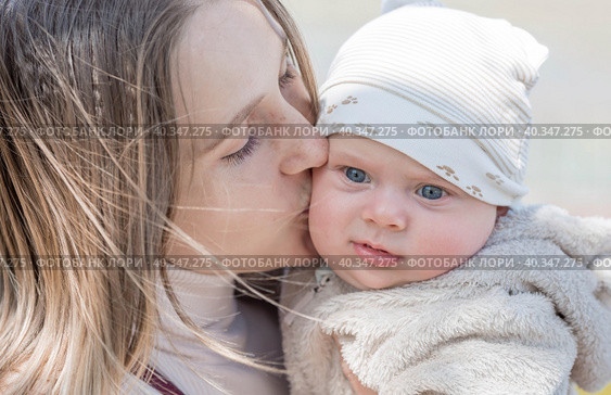 A young mother holds a charming little son in her arms. The kid looks at the camera and smiles. Portrait of a beautiful chubby 4-month-old baby. Стоковое фото, фотограф Photojuli / Фотобанк Лори