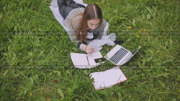 A young student with notebooks and a laptop lying on the grass. Стоковое видео, видеограф Mikhail Davidovich / Фотобанк Лори