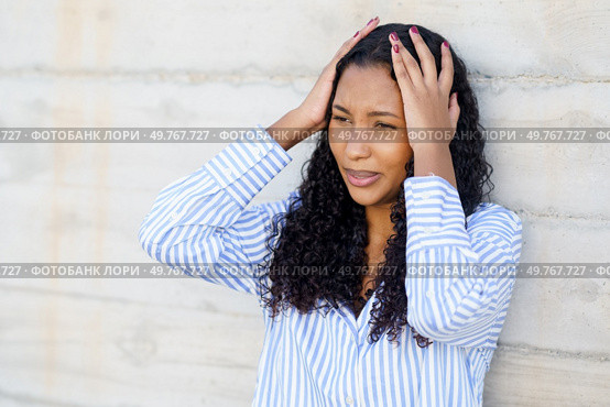 A young woman is clearly showing signs of stress and anxiety, as she holds her head in her hands while leaning against a textured wall, revealing her emotional state and internal struggle. A Stressed Young Woman is Holding Her Head in Discomfort Against a Wall, Struggling With Tension. Стоковое фото, агентство Ingram Publishing / Фотобанк Лори