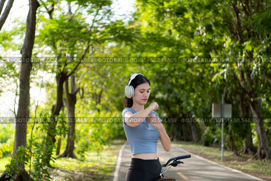 A young woman listens to music while wearing headphones. While cycling in the park, take a hydration break. Стоковое фото, агентство Ingram Publishing / Фотобанк Лори