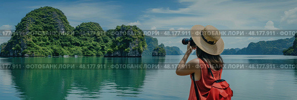 A young woman with a camera admires the serene beauty of Halong Bay surrounded by lush greenery. Стоковое AI-изображение, AI-художник Данила Большаков / Фотобанк Лори