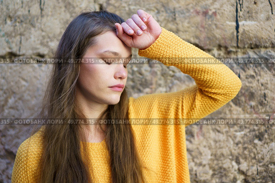 A young woman with flowing, beautiful hair, clad in a bright, vibrant yellow sweater, stands gracefully against an aged stone wall, evoking a sense of introspection, tranquility, and calmness. A contemplative young woman wearing a bright yellow sweater stands gracefully against a stone wall. Стоковое фото, агентство Ingram Publishing / Фотобанк Лори