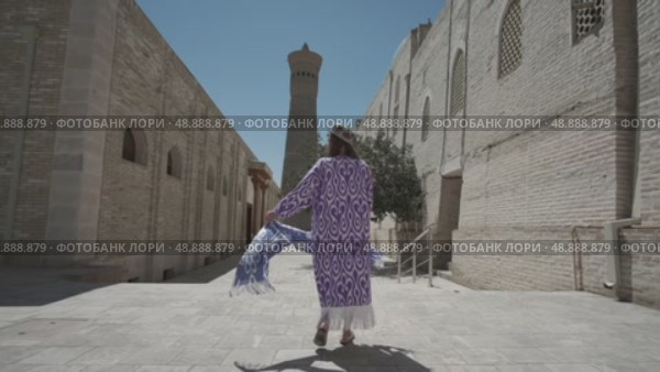 A young woman with long hair in an oriental robe and a skullcap walks through an ancient oriental city. Стоковое видео, видеограф Aleksey Kidisyuk / Фотобанк Лори