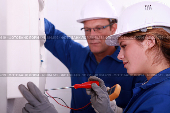 a young woman working on an electricity meter accompanied with a 45 years old man, both are wearing blue jumpsuites. Стоковое фото, агентство Ingram Publishing / Фотобанк Лори