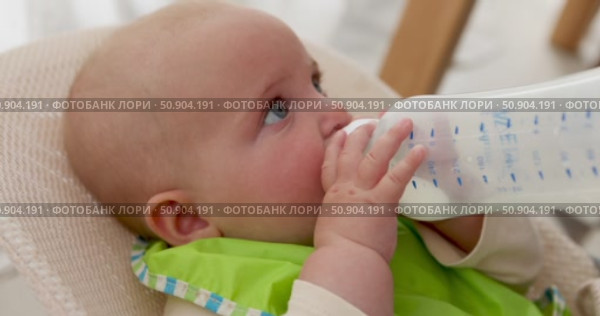 Adorable baby enjoying milk from bottle in high chair. Стоковое видео, видеограф Ekaterina Demidova / Фотобанк Лори