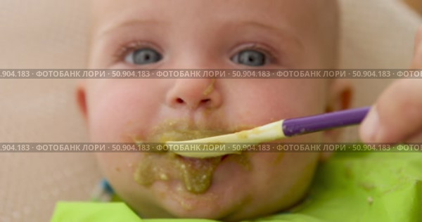 Adorable baby making a mess eating green puree. Стоковое видео, видеограф Ekaterina Demidova / Фотобанк Лори