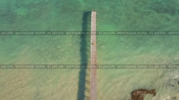Aerial of long wooden dock with lone figure walks a sunlit pier over tranquil crystal clear waters in Yucatan Mexico. Стоковое видео, видеограф Igor Tichonow / Фотобанк Лори