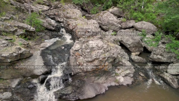 Aerial perspective showcases a beautiful waterfall flowing over rocks, surrounded by vibrant greenery, creating a peaceful and natural atmosphere in the landscape. Стоковое видео, видеограф Ирина Ручушкина / Фотобанк Лори