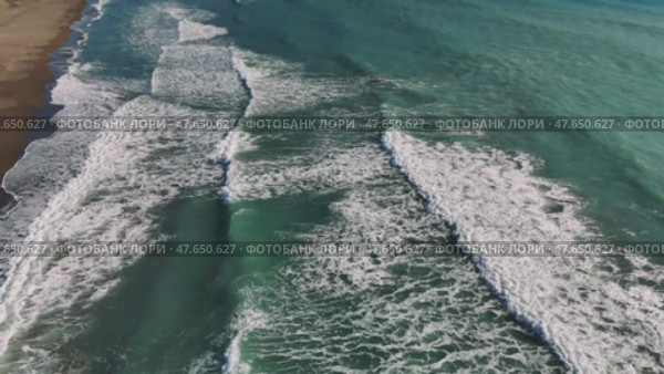 Aerial view capturing rhythmic turquoise waves rolling, breaking against golden sandy shoreline, showcasing powerful oceanic motion. Стоковое видео, видеограф ILIA GOROKHOV / Фотобанк Лори