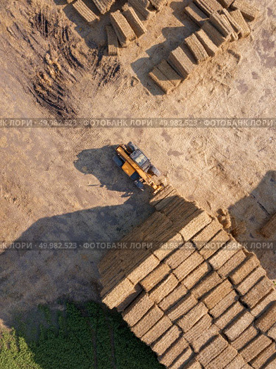 Aerial view from drone into the stack of straw after harvesting the grain. Natural ecological fuel and fertilizers for agricultural work.. The loader stacks bales of straw into the stack after harvesting the grain. Top view. Стоковое фото, агентство Ingram Publishing / Фотобанк Лори