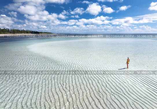 Aerial view of alone young woman on the sandbank in ocean, white sand, blue sea during low tide on sunny summer day in Zanzibar island. Top view of girl, sand spit, bay, clear water, sky with clouds. Стоковое фото, агентство Ingram Publishing / Фотобанк Лори