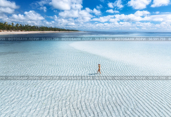 Aerial view of alone young woman on the sandbank in ocean, white sand, blue sea during low tide on sunny summer day in Zanzibar island. Top view of girl, sand spit, bay, clear water, sky with clouds. Стоковое фото, агентство Ingram Publishing / Фотобанк Лори