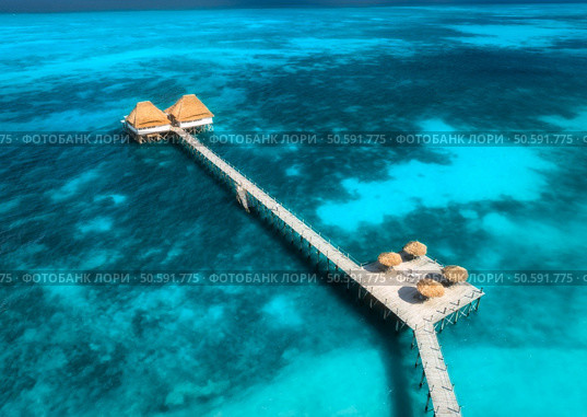 Aerial view of bungalow, jetty, sandy beach, ocean on summer sunny day. Restaurant on the blue sea. Top drone view of wooden hotel, azure water. Luxury resort in Zanzibar. Tropical background. Travel. Стоковое фото, агентство Ingram Publishing / Фотобанк Лори