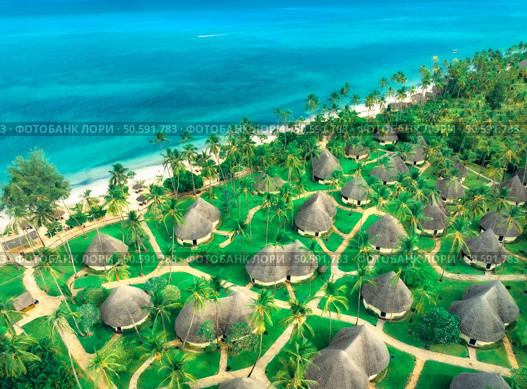 Aerial view of green palms, bungalows, grass, sandy beach, blue ocean at sunset in summer. Top view of wooden houses, sea with azure water, palms. Luxury resort in Zanzibar. Tropical background. Стоковое фото, агентство Ingram Publishing / Фотобанк Лори
