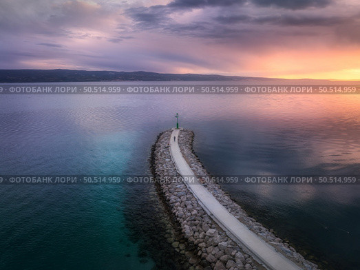 Aerial view of lighthouse on the pier at colorful sunset in summer. Top drone view of lighthouse on jetty, blue sea and cloudy sky with sunlight. Landscape. Adriatic sea, Omis, Croatia. Travel	. Стоковое фото, агентство Ingram Publishing / Фотобанк Лори