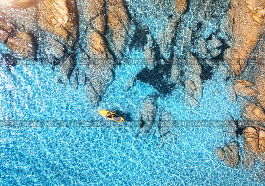 Aerial view of man on floating sup board on blue sea, rocky beach at sunset in summer in Sardinia, Italy. Tropical landscape. Kayak on crystal clear water and stones. Top view from drone of canoe. Стоковое фото, агентство Ingram Publishing / Фотобанк Лори