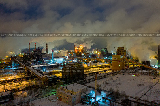 Aerial view of metallurgical plant blast furnace at night with smokestacks and fire blazing out of the pipe. Industrial panoramic landmark with blast furnance of metallurgical production. Стоковое фото, фотограф Евгений Ткачёв / Фотобанк Лори
