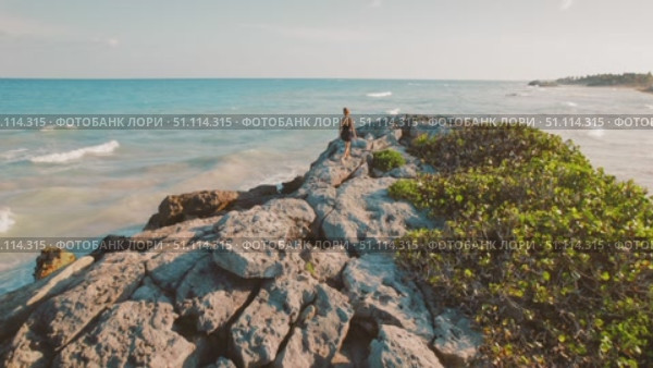 Aerial view of woman walking on rocky shore and looking at ocean in Tulum Yucatan. Стоковое видео, видеограф Ольга Сухарева / Фотобанк Лори